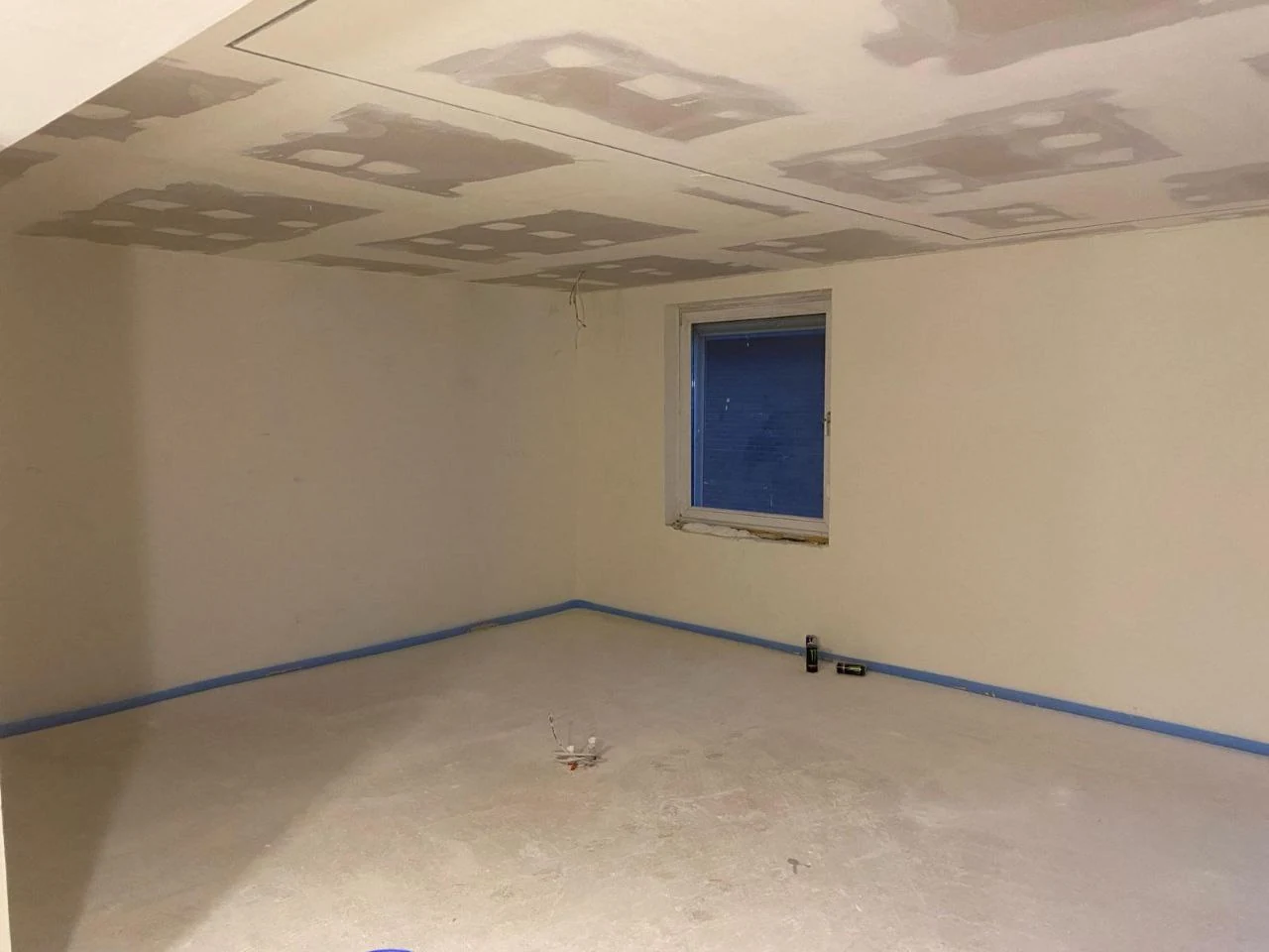 Leerer Wohnraum mit Fenster und neuer Trockenbaudecke, an der Fugen und Schraubenköpfe verspachtelt sind
