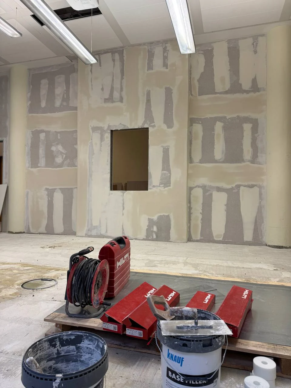 Große verspachtelte Trockenbauwand mit rechteckiger Wandöffnung in einer Gewerbefläche, davor Werkzeugkoffer und Eimer