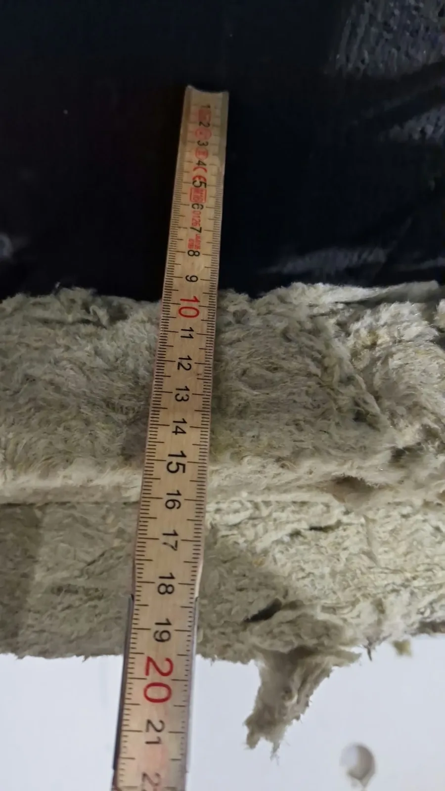 Zollstock misst die Dicke einer Mineralwolle-Dämmschicht im Hohlraum einer abgehängten Decke