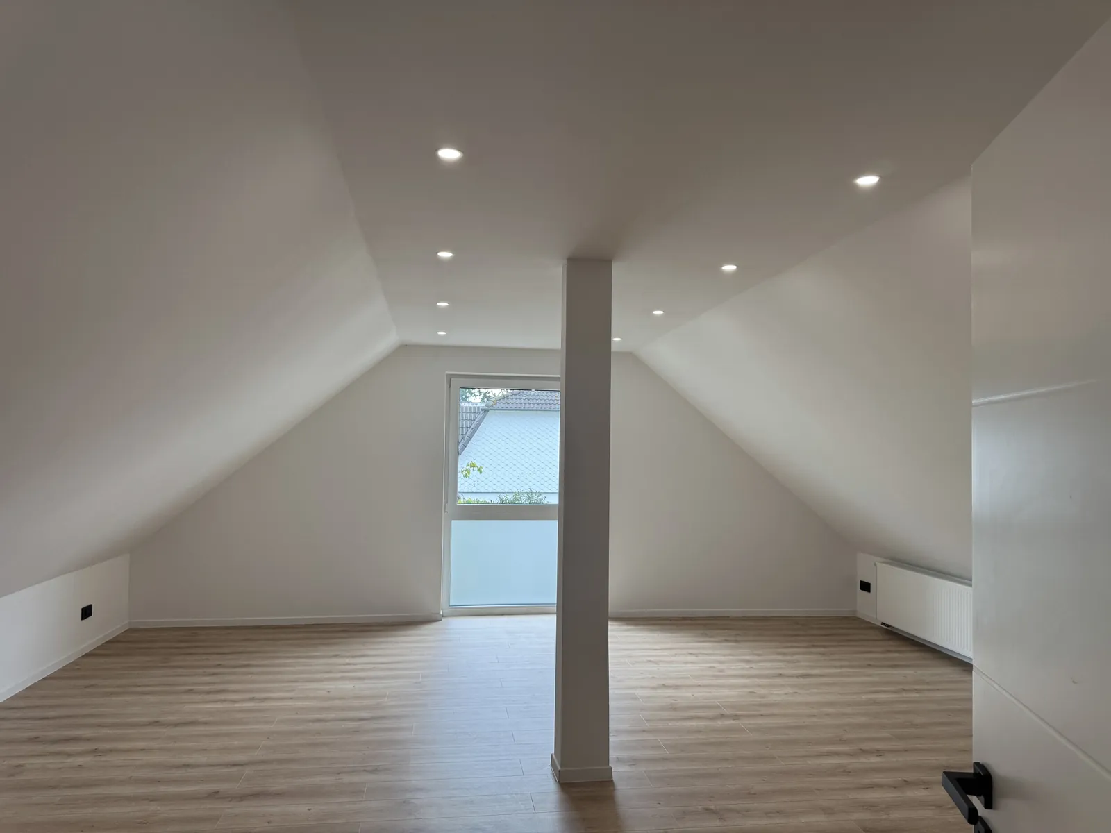 Fertig ausgebautes Dachgeschoss in Hamburg-Poppenbüttel: heller Wohnraum mit weißen Dachschrägen, Einbauspots, Fenstertür, Heizkörper und Boden in Holzoptik