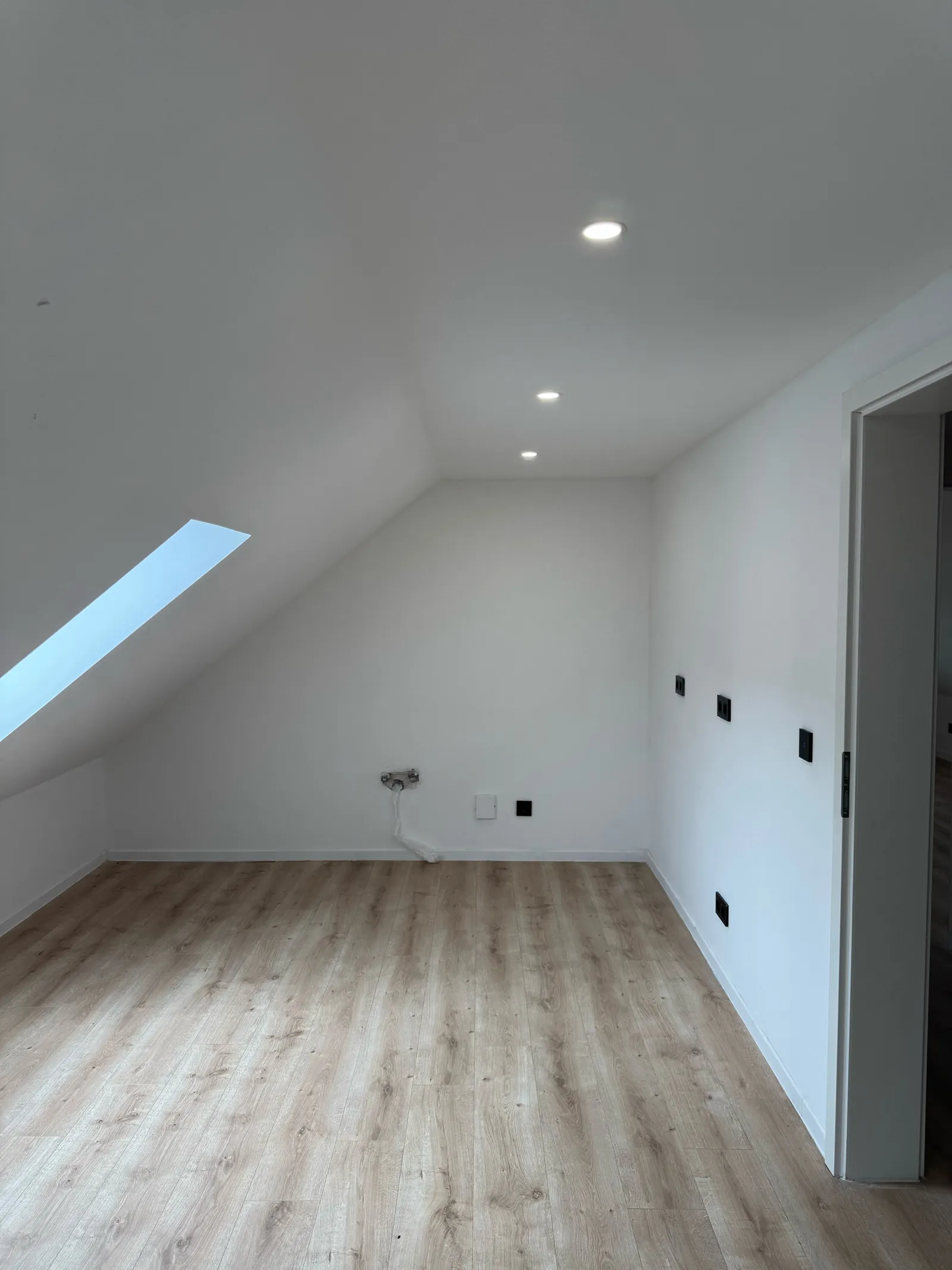 Fertiges Zimmer im Dachgeschoss mit Dachflächenfenster, Steckdosen, Türöffnung und Boden in Holzoptik