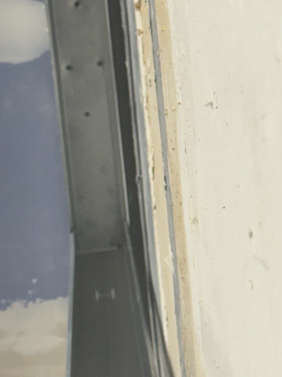 Nahaufnahme des Randanschlusses einer entkoppelten Unterdecke: Metallprofil der Unterkonstruktion mit Abstand zur Wand und Fuge zur Beplankung